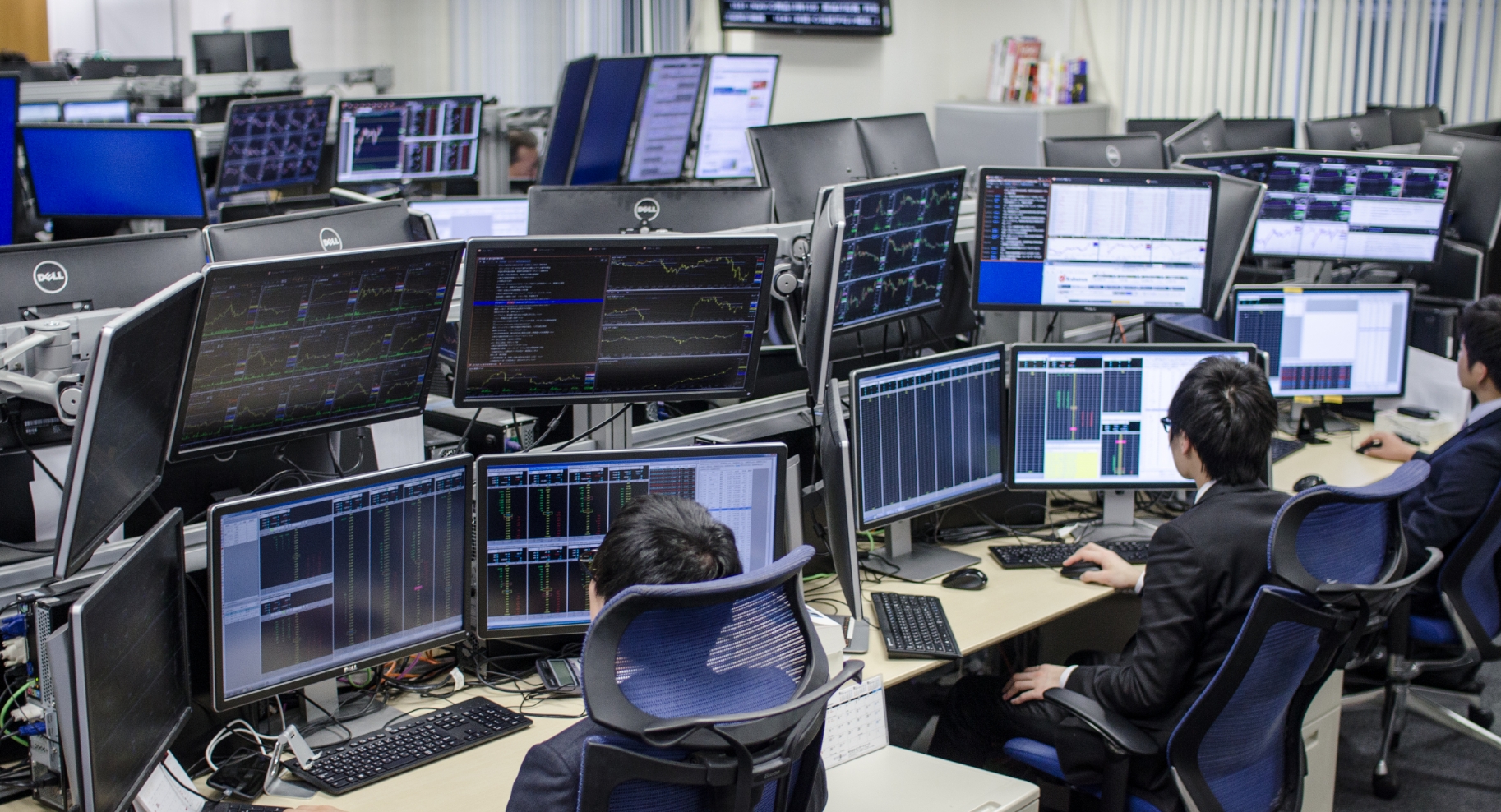 複数のモニターで取引グラフを分析している社内