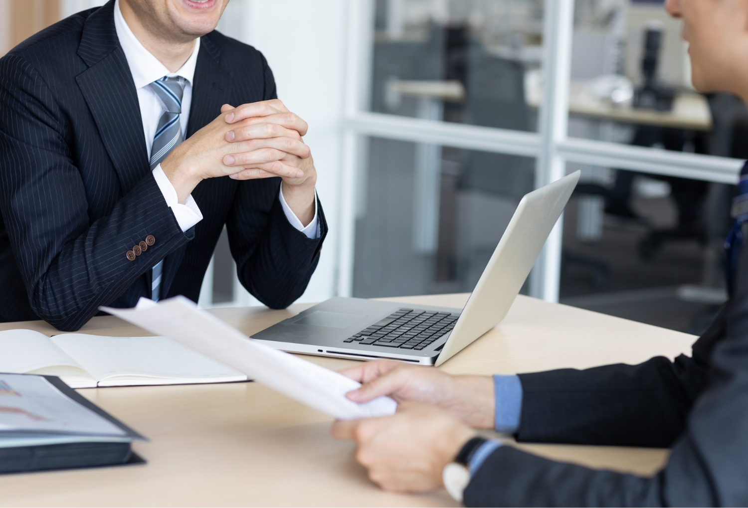 ノートパソコンと資料を前に打ち合わせをする2人の社員