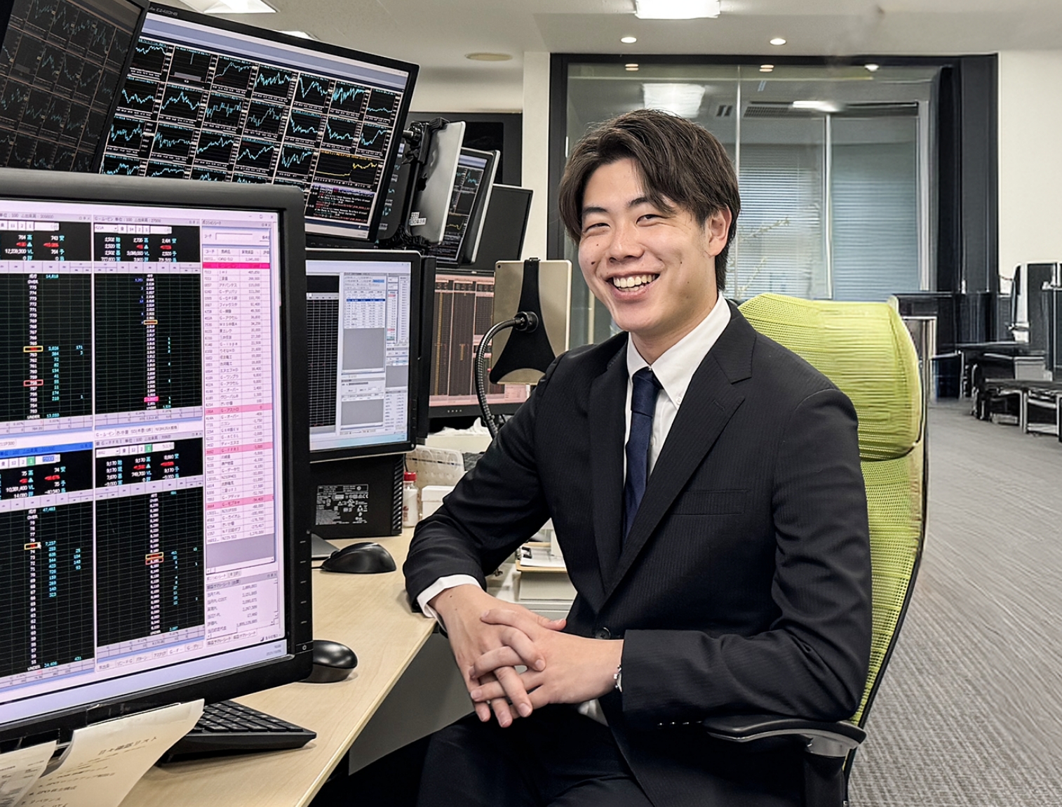 スーツ姿でモニター数台の前に座るディーラー職の男性社員