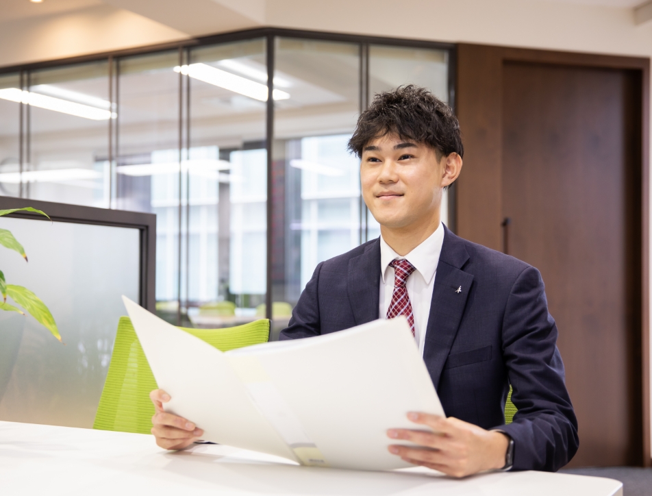 紙の書類を持ち、クライアントに説明をするスーツの男性
